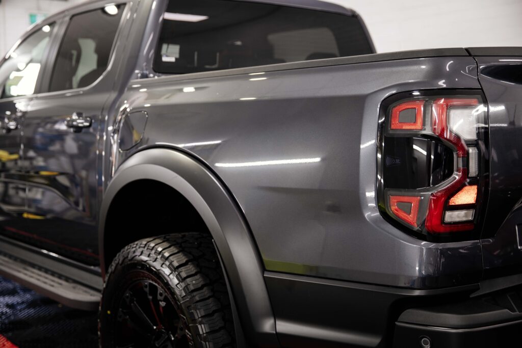 Close-up of the rear of a silver 2024 Ford Ranger Raptor truck with a black Ford emblem, highlighting the glossy paint finish protected by a nearly invisible coat of paint protection film (PPF).